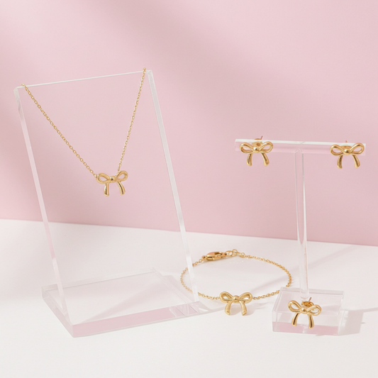 Gold jewelry set with bow accents on a pink background